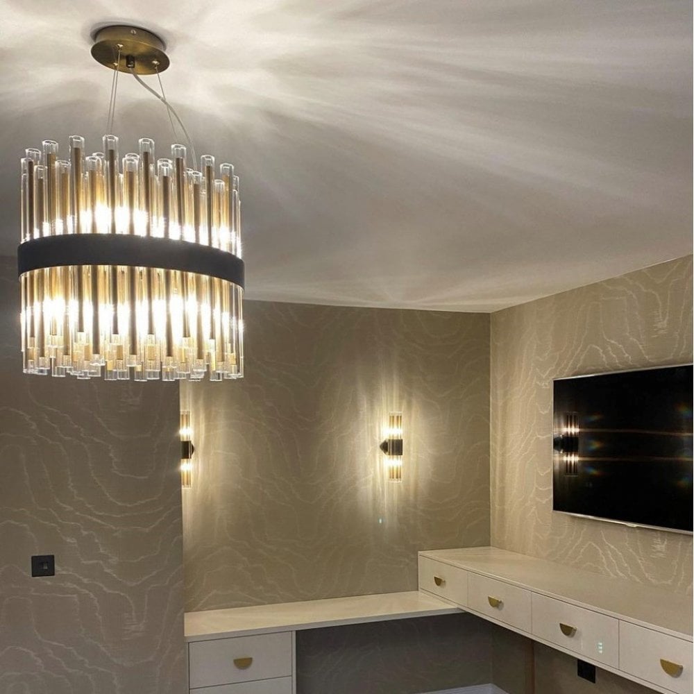 A living room with a round gold and glass chandelier and two matching wall sconces.