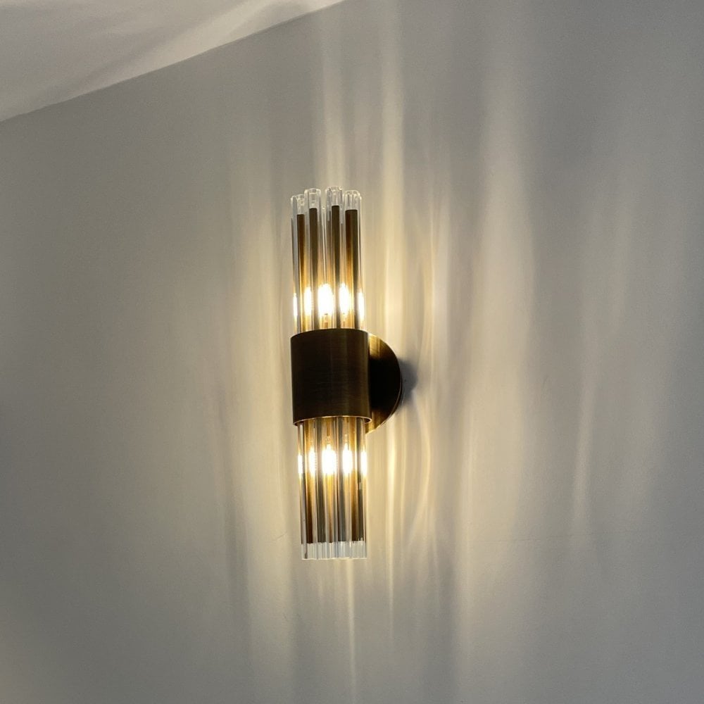 An illuminated black and clear glass rod wall sconce casting light streaks on a wall.