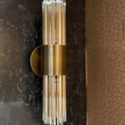 A brass wall sconce with clear glass rods mounted on a dark marble wall.