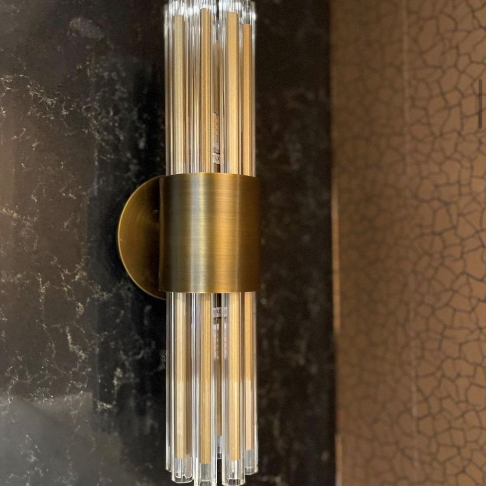 A brass wall sconce with clear glass rods mounted on a dark marble wall.