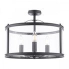 A modern black semi-flush ceiling light with a clear glass drum shade and three visible bulbs.