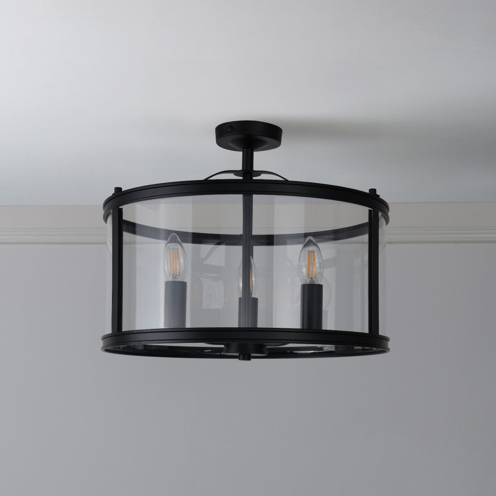 A stylish semi-flush ceiling light in black finish, featuring a clear glass drum and three bulbs.