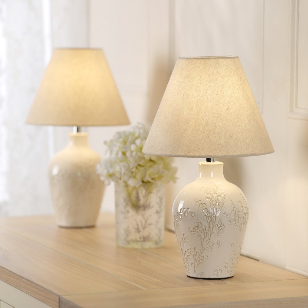 Two elegant cream table lamps on a wooden dresser with a white floral centerpiece.