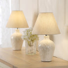 Two elegant cream table lamps on a wooden dresser with a white floral centerpiece.