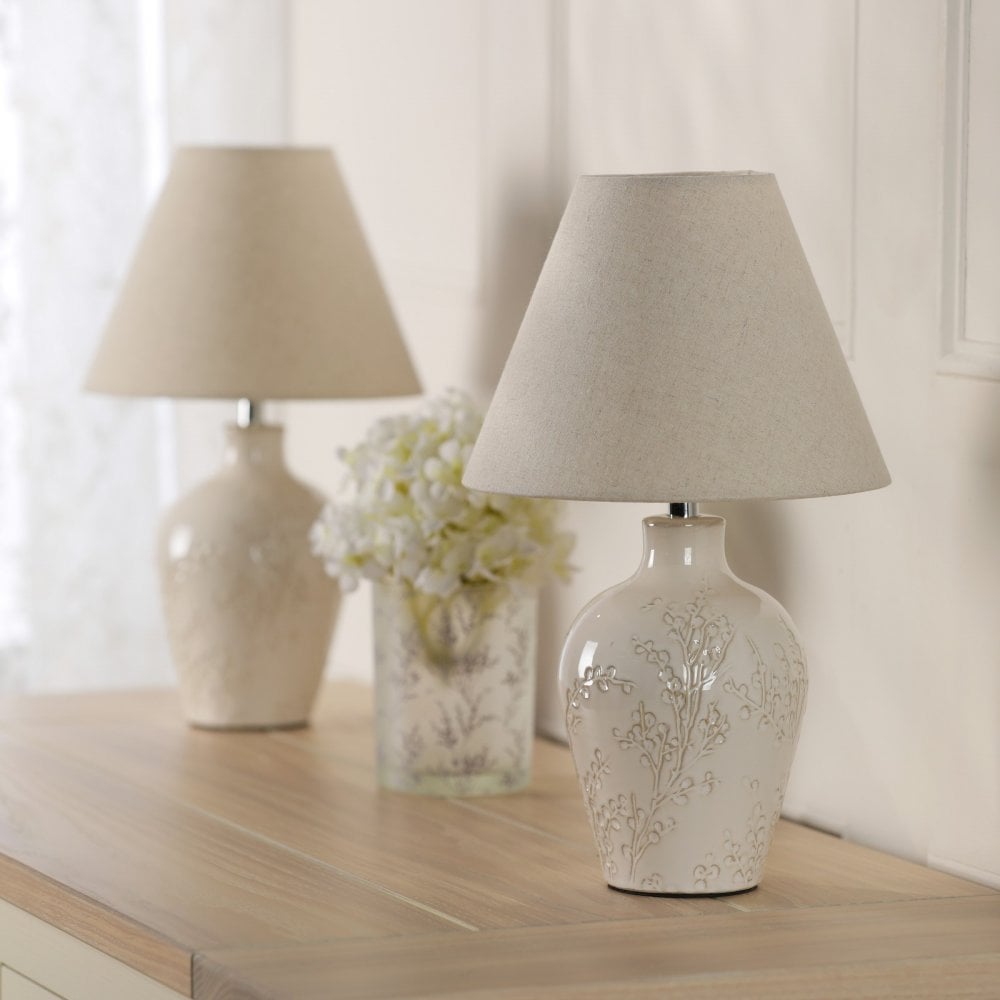 Two elegant cream table lamps on a wooden dresser with a white floral centerpiece.