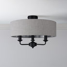 A semi-flush mount ceiling light with a grey fabric drum shade and three exposed black bulbs.