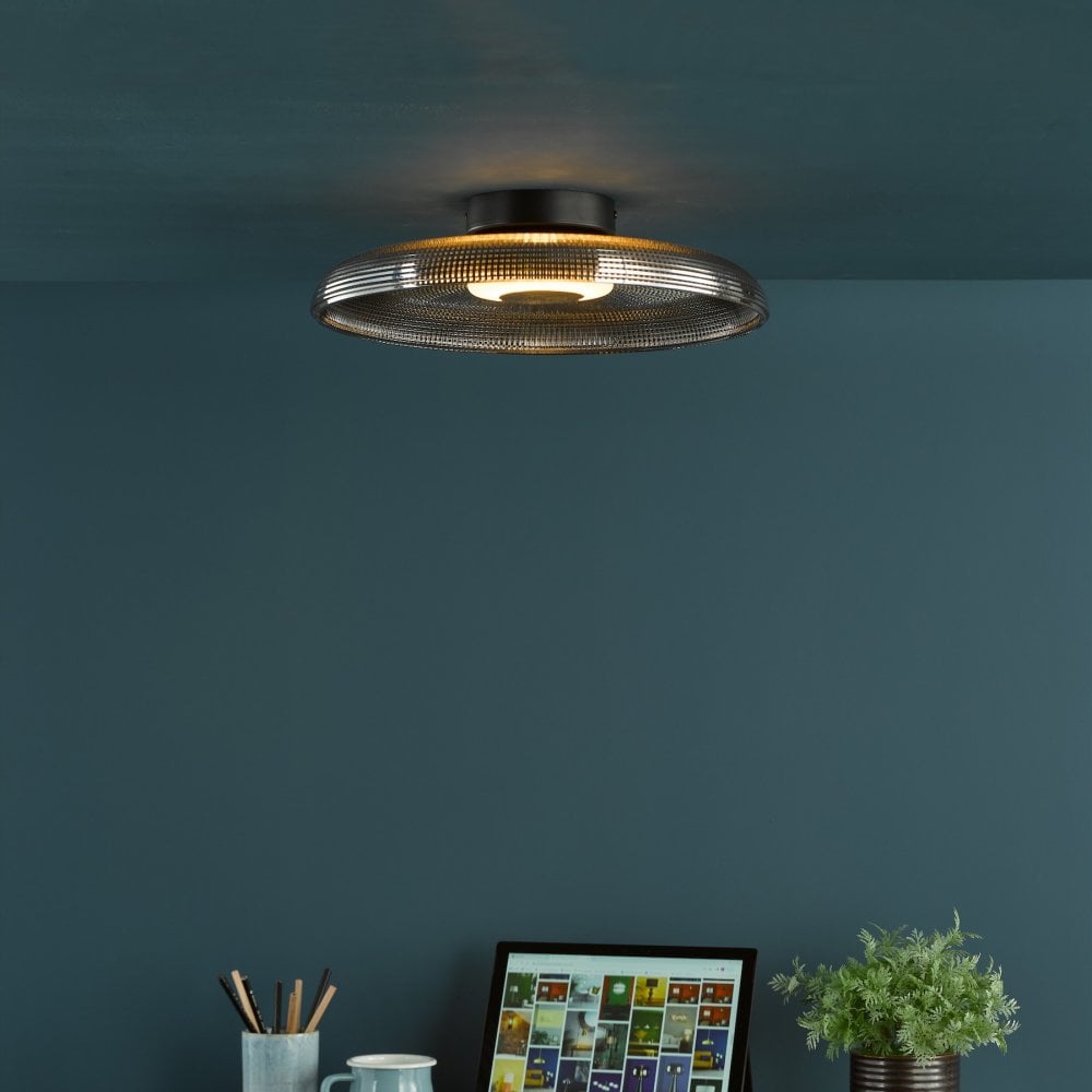 A ceiling light with a dark gray glass shade illuminates a dark blue room with a desk below.