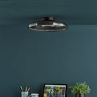 A minimalist ceiling light with a dark gray glass shade is installed in a dark blue room.
