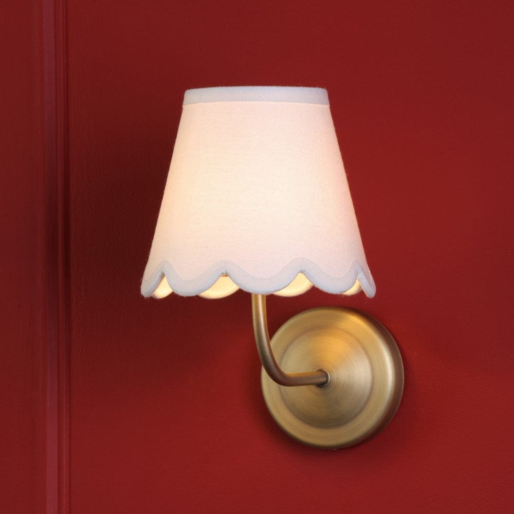 Illuminated brass wall sconce with a white scalloped shade on a red wall.