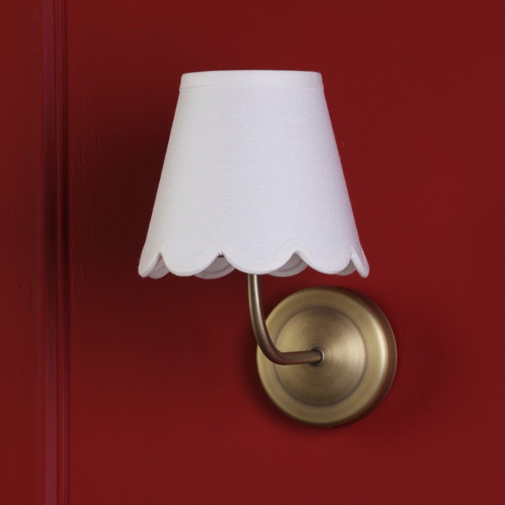 Brass wall sconce with a white scalloped shade against a red wall.