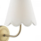 Close-up of a brass wall sconce with a white scalloped fabric shade.