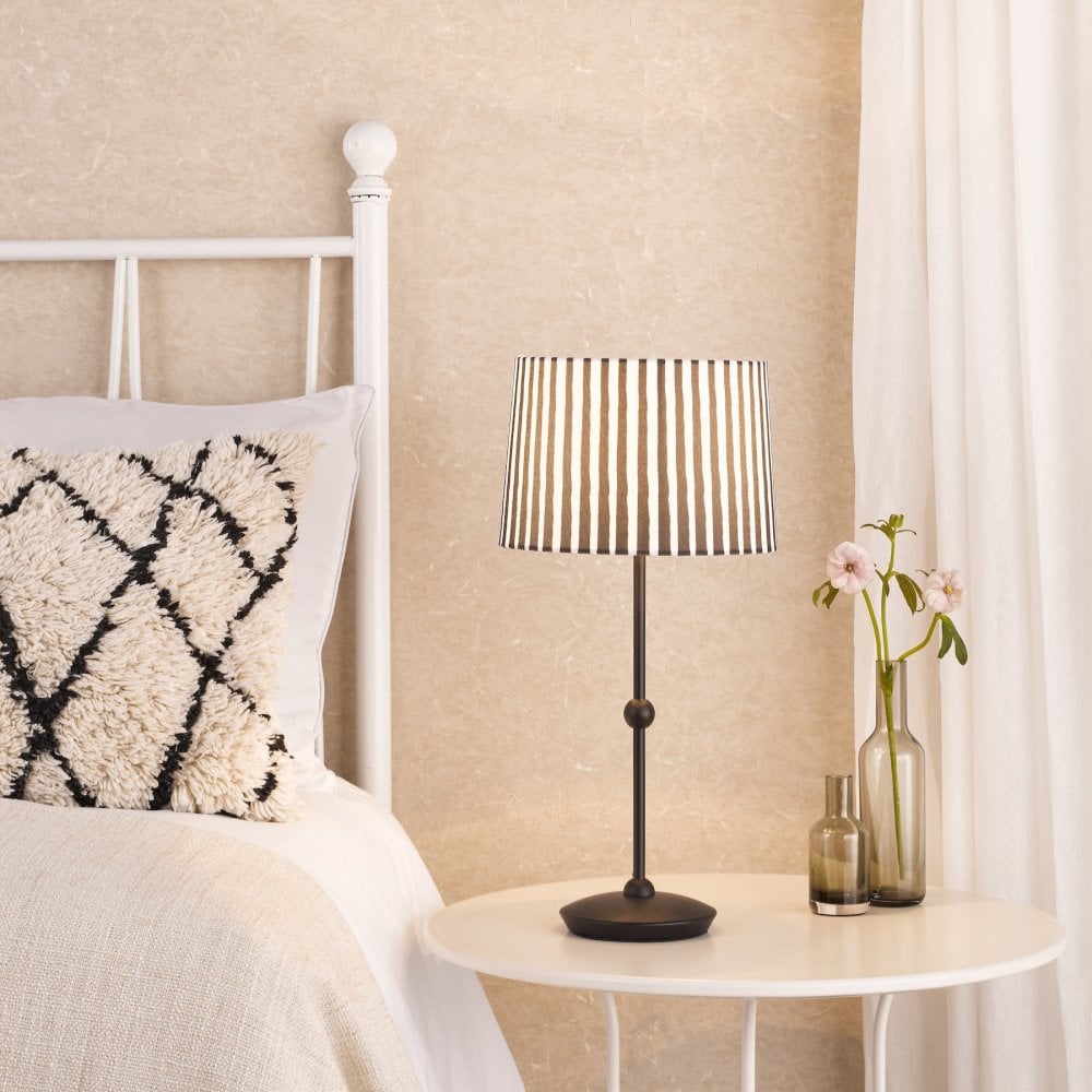 A black table lamp with a striped shade next to a bed.