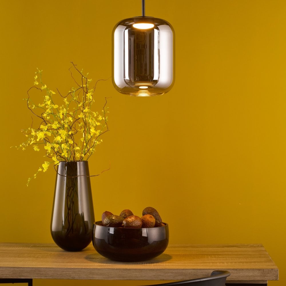 A modern pendant light illuminating a tabletop with a vase and bowl against a yellow wall.