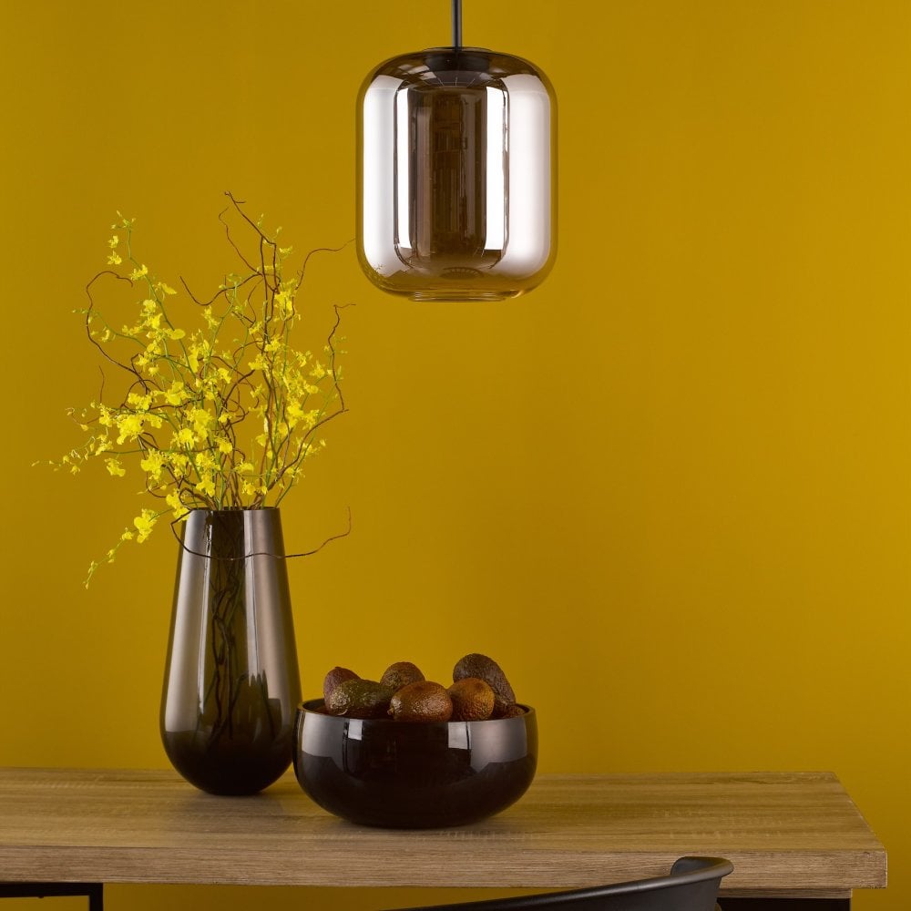 A modern pendant light illuminating a tabletop with a vase and bowl against a yellow wall.