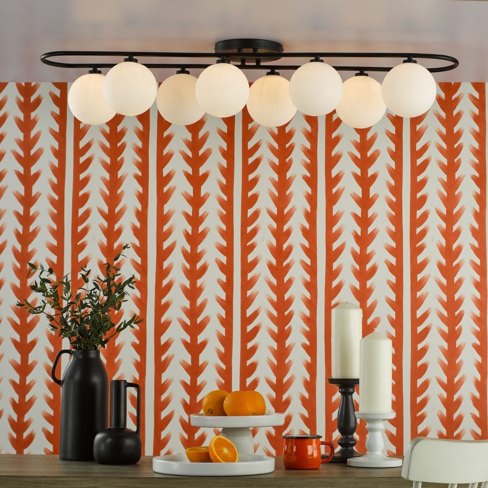 An oval-shaped light fixture with eight white globes illuminates a dining table.