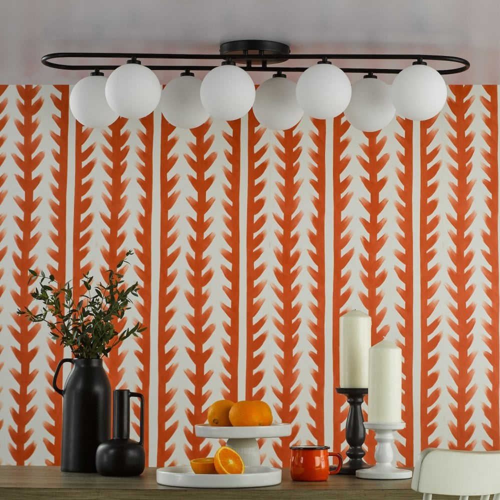 An oval-shaped light fixture with eight white globes illuminates a dining table.