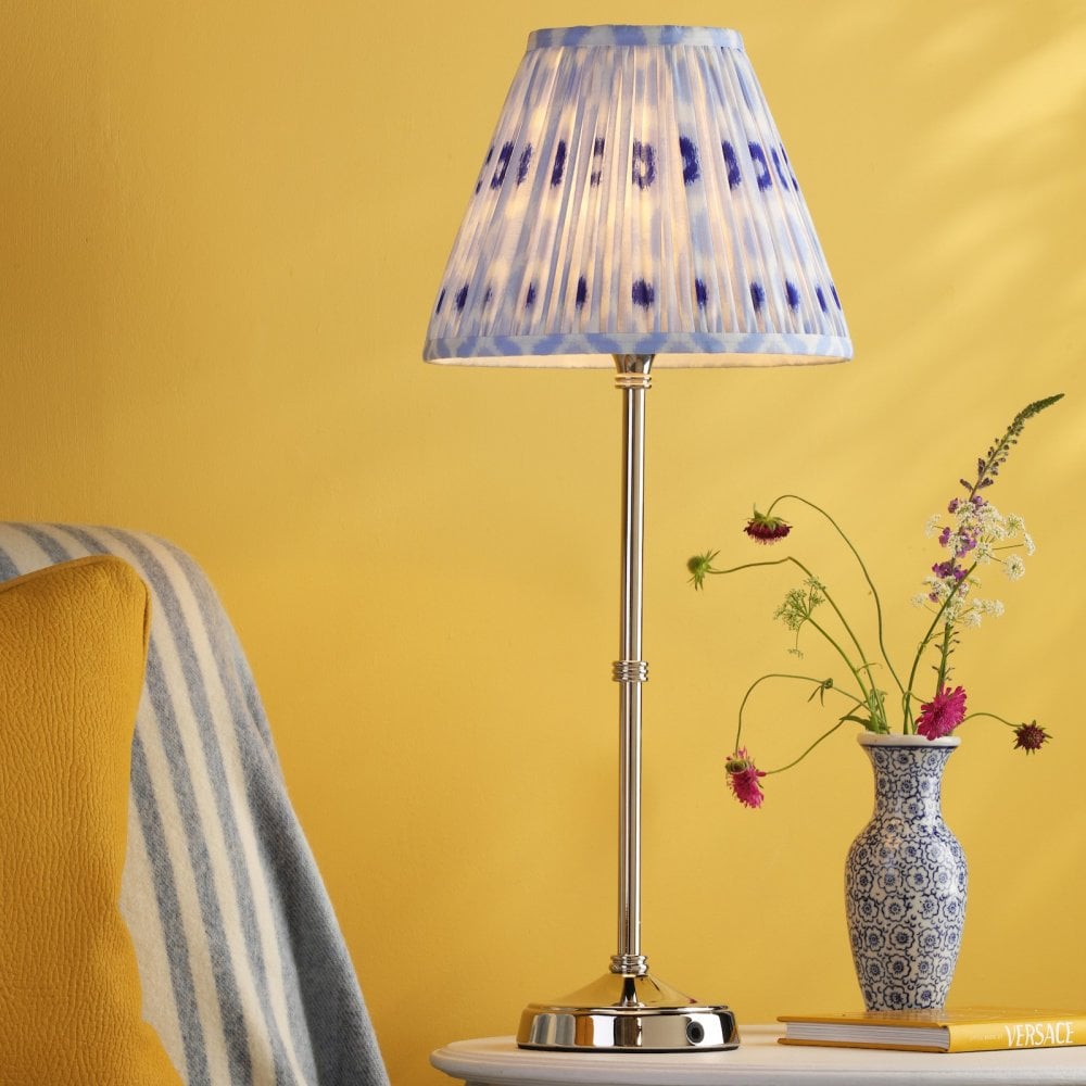 A white table lamp with a blue and white patterned lampshade, on a table with a yellow wall.
