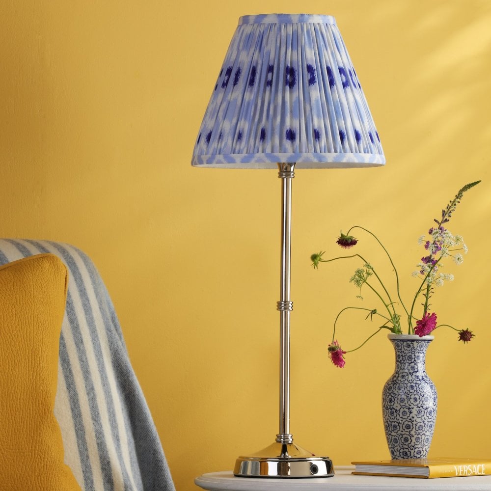 A white table lamp with a blue and white patterned lampshade, on a table with a yellow wall.