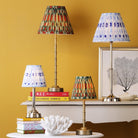Four table lamps with patterned shades on tables against a yellow wall.