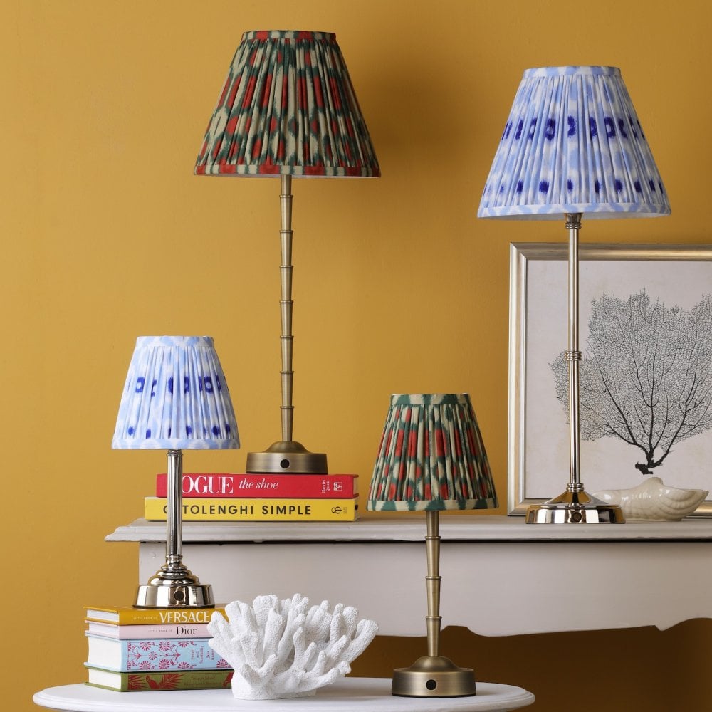 Four table lamps with patterned shades on tables against a yellow wall.