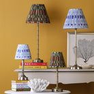 Four table lamps with patterned shades on tables against a yellow wall.
