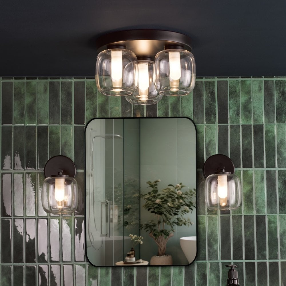 A bathroom with green tiles, a mirror, and a matching three-light ceiling fixture and sconces.