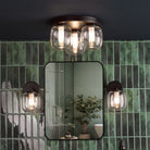 A bathroom with green tiles, a mirror, and a matching three-light ceiling fixture and sconces.