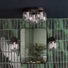 A bathroom with green tiles, a mirror, and a matching three-light ceiling fixture and sconces.