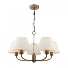 A five-light chandelier with white shades and an antique brass finish.