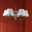 A five-light chandelier with grey shades and an antique brass finish on a red paneled wall.