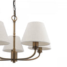 Close-up of a five-light chandelier with textured off-white shades and an antique brass finish.