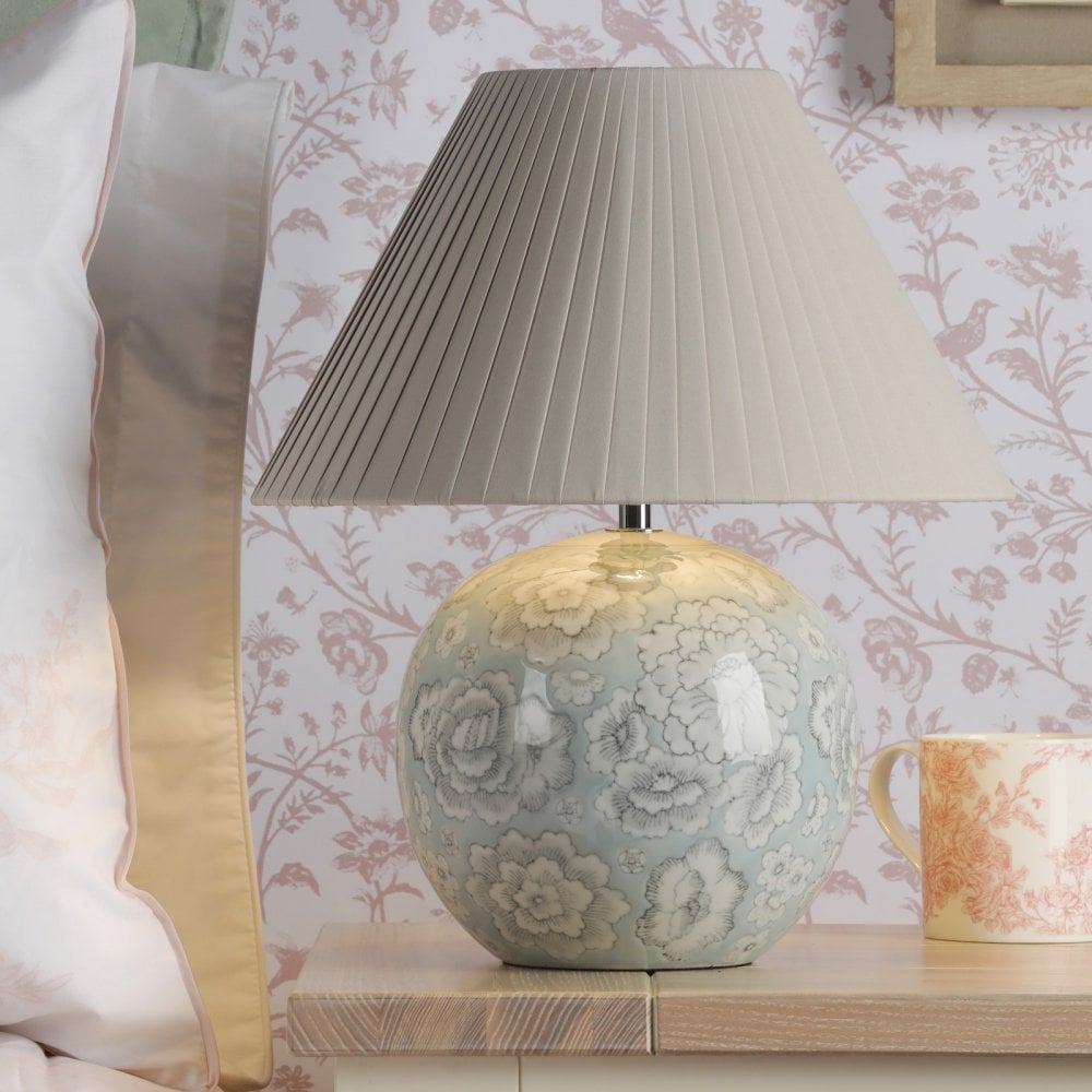 A white and blue floral globe lamp is placed on a nightstand with a white lampshade.