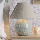 A white and blue floral globe lamp is placed on a nightstand with a white lampshade.
