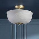 A semi-flush ceiling light with a brass base and a white marbled glass shade, unlit.
