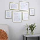 A gallery wall arrangement of six gold picture frames in various sizes on a white wall.