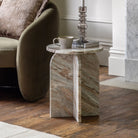 Round marble side table with an arched base holding a cup and book.