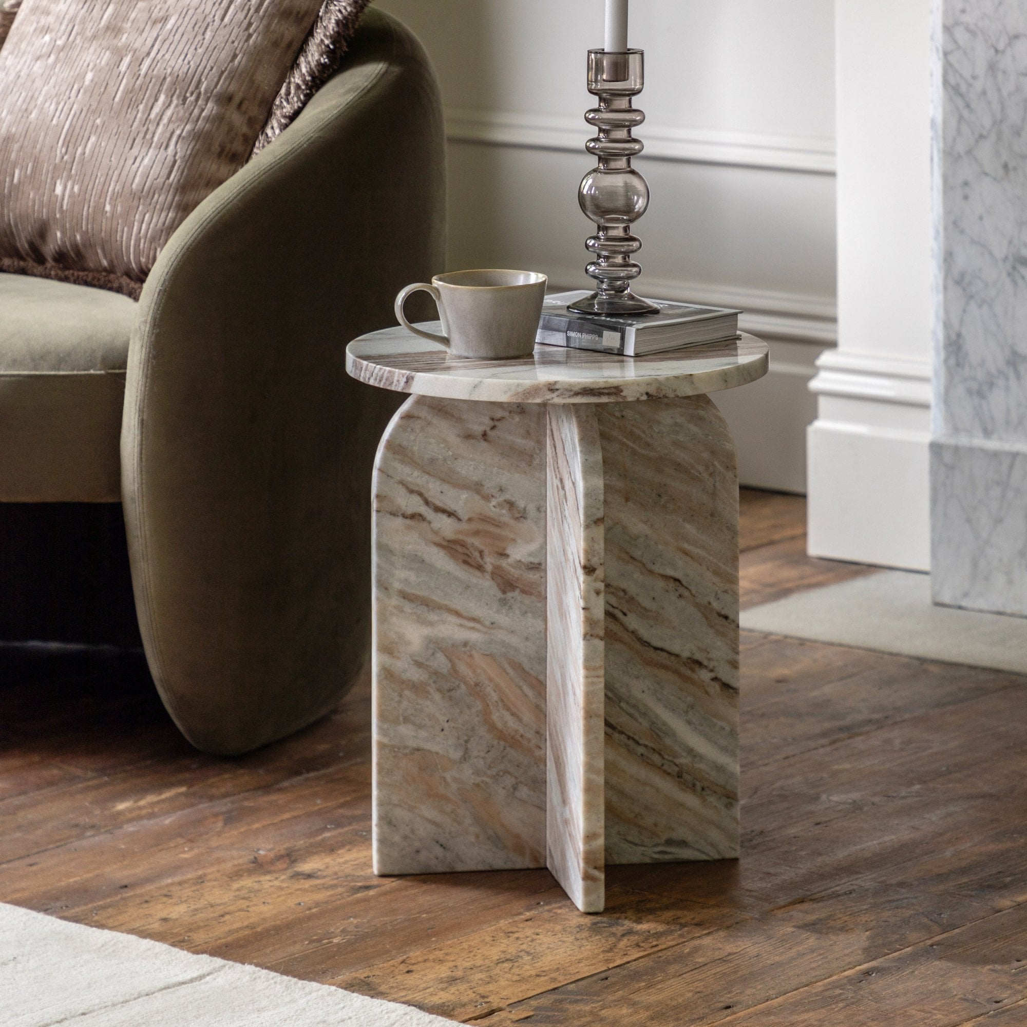 Round marble side table with an arched base holding a cup and book.