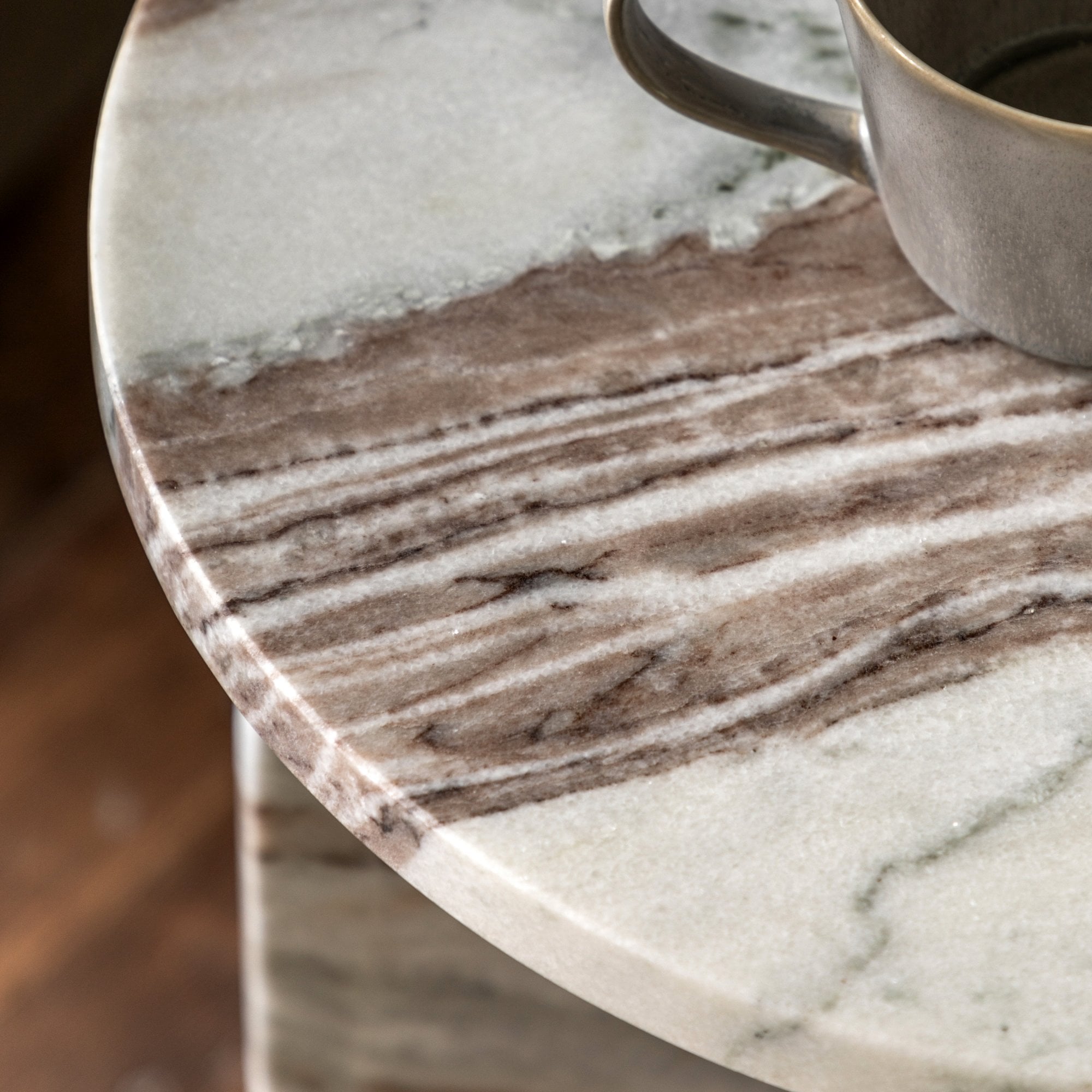 Close-up of the round marble tabletop with brown and white veining, holding a cup.