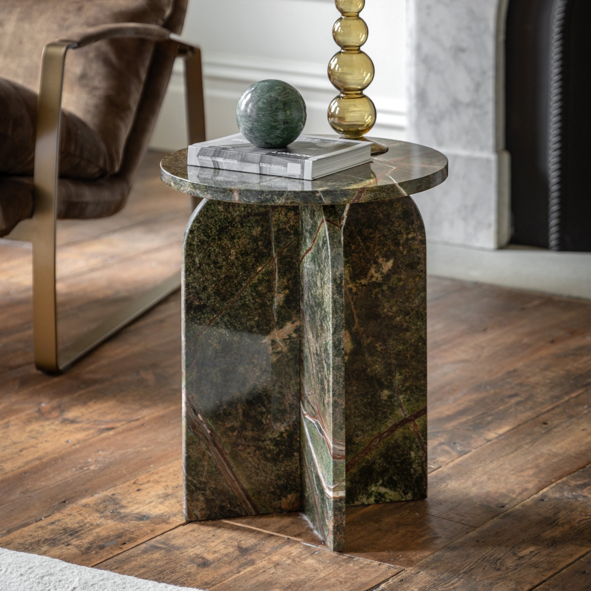 Green marble side table with rounded base in a living room next to a brown armchair.