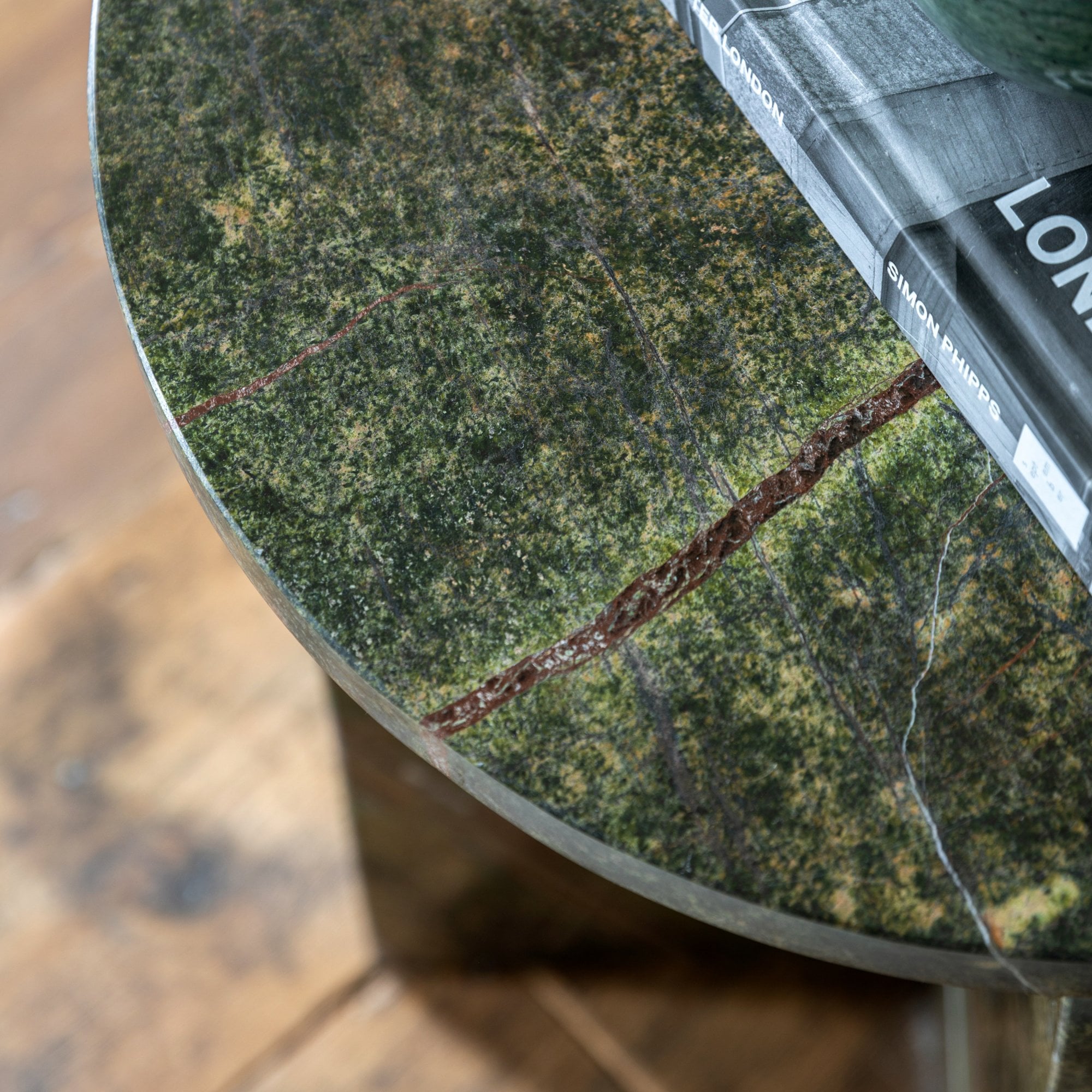 Close-up of a green marble tabletop with natural reddish-brown veins, holding a book.