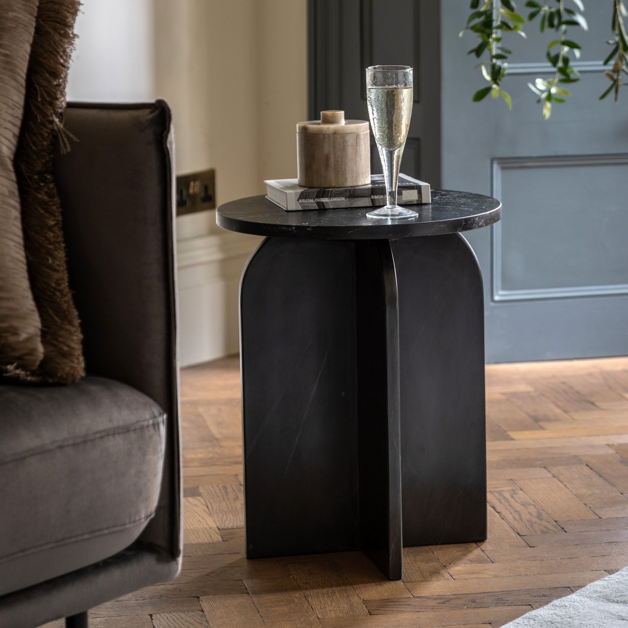A black marble side table with a glass of champagne and a decorative pot on top.