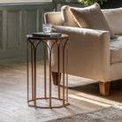 A sleek, bronze side table with a glass top, next to a comfy beige sofa in a modern living room.