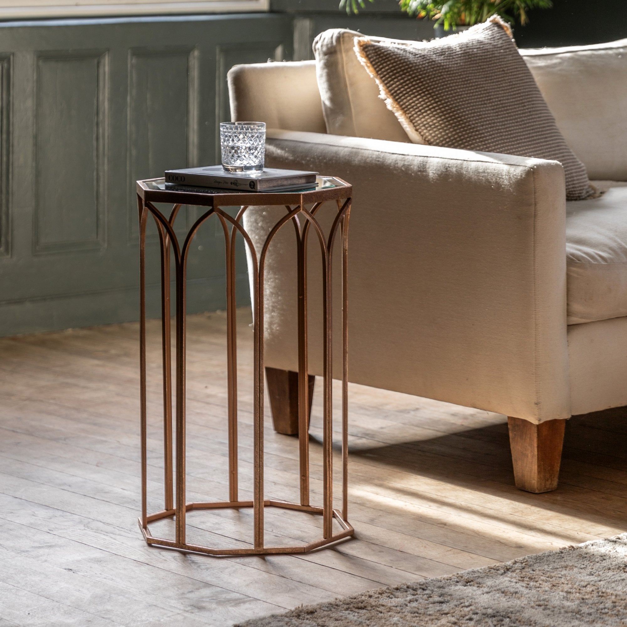 A sleek, bronze side table with a glass top, next to a comfy beige sofa in a modern living room.
