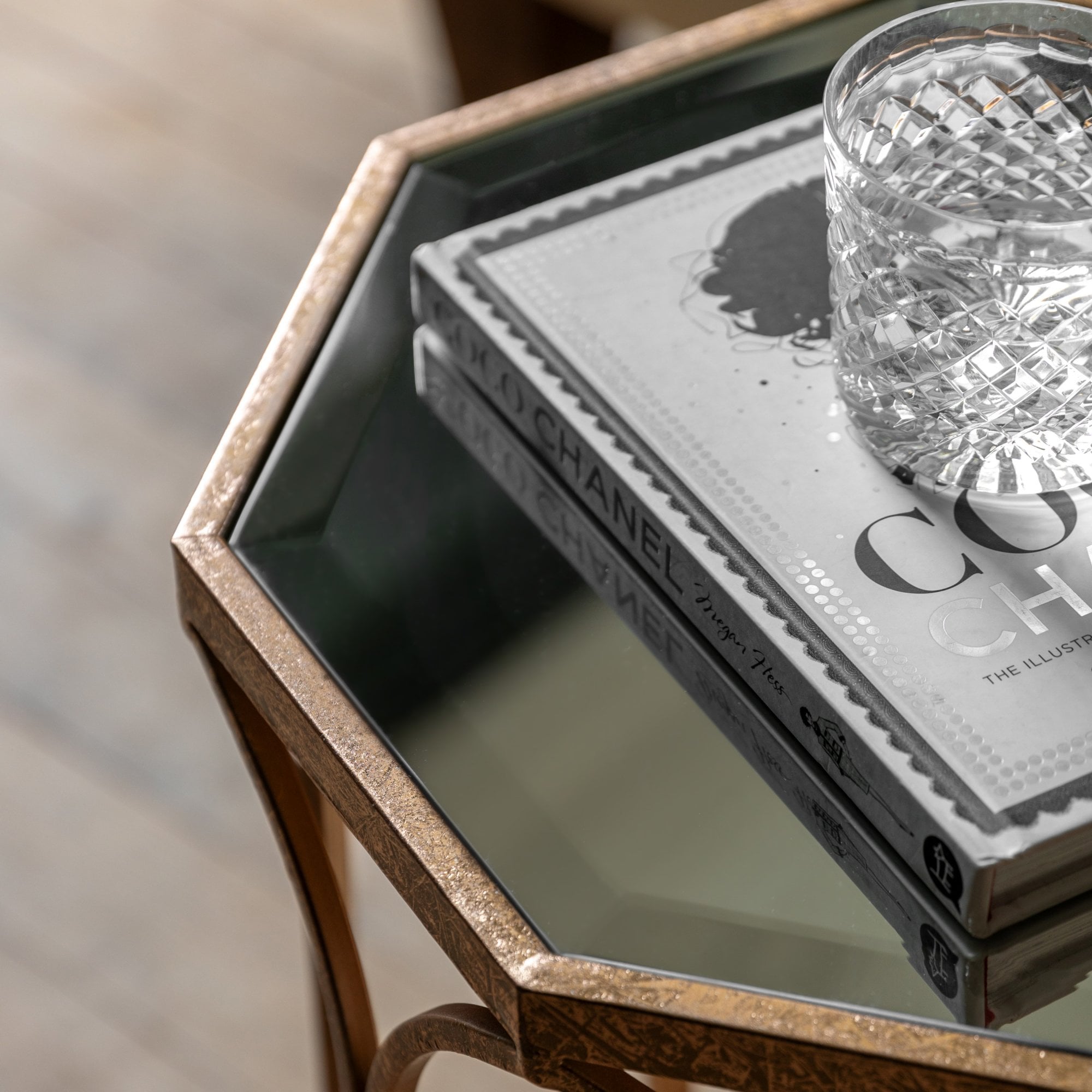 Close-up of the side table's glass top with two books and a crystal glass.