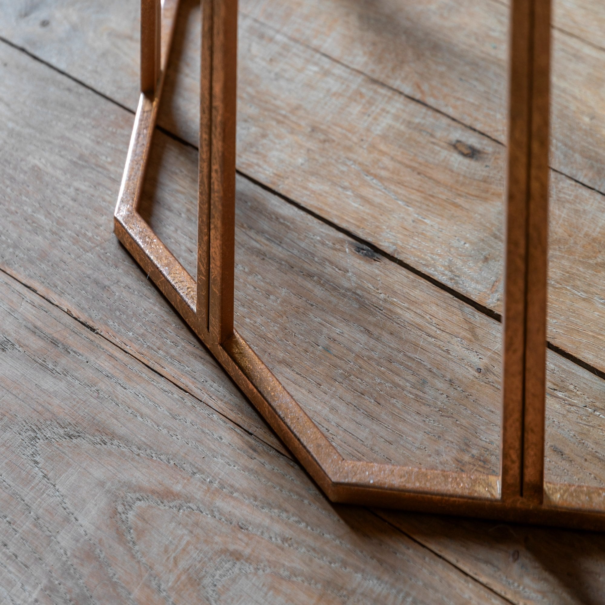 Detail of the bronze metal base of the side table on a light wooden floor.