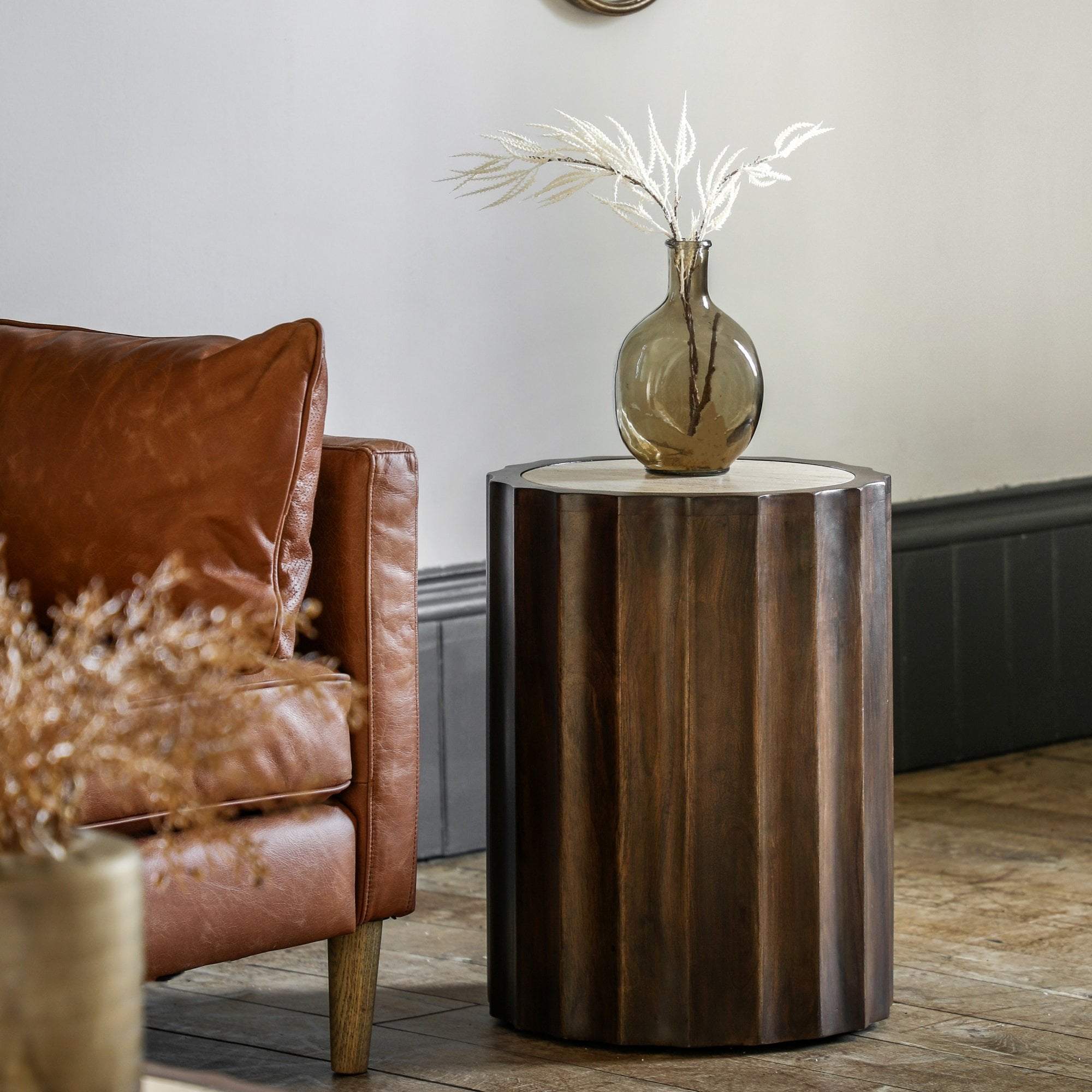 A round wooden side table with a light-colored top sits next to a brown leather sofa.