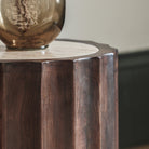 A close-up of the dark wood fluted side and light stone top of a round table.