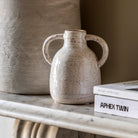A small, light-colored ceramic vase with two handles sits on a white marble surface.