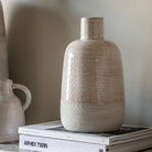 A beige glazed vase with a textured matte base stands on books.