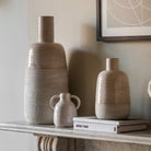 A collection of textured beige vases and a pot adorn a mantelpiece.